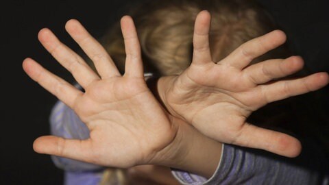 Eine Person hält beide Hände schützend vor ihren Kopf