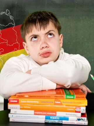 Junge mit fragendem Blick sitzt vor einer Schultafel mit Deutschlandumriss, nach Bundesländern aufgeteilt, darüber die Farben Schwarz-Rot-Gold.