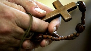 Mann hält Rosenkranz mit Kreuz in den Händen