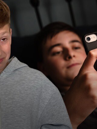 Trauriger Schüler im Vordergrund, im Hintergrund ein Kind am Smartphone