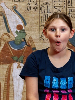 Im Hintergrund eine altägyptische Zeichnung auf Papyrus, im Vordergrund ein erstauntes Mädchen